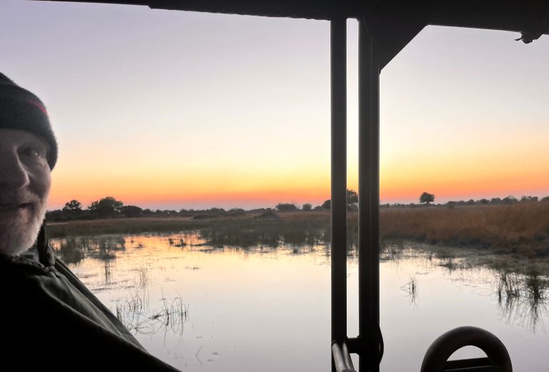 Botswana safari: guest in game vehicle at sunrise over floodplain