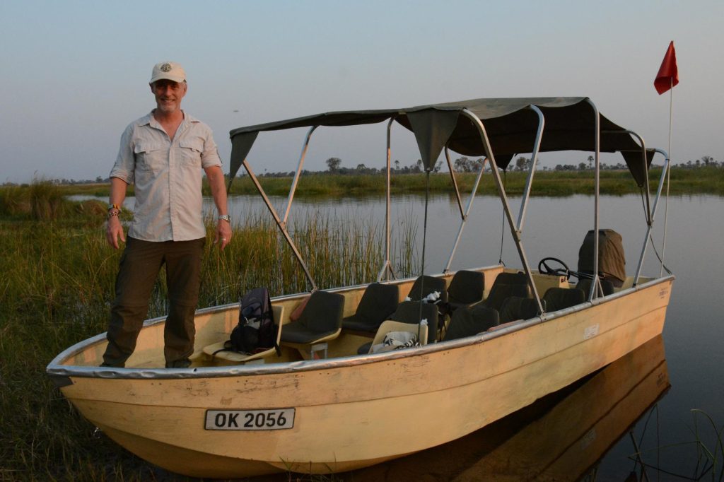 Botswana safari: man standing in canopied motorboat at delta shore