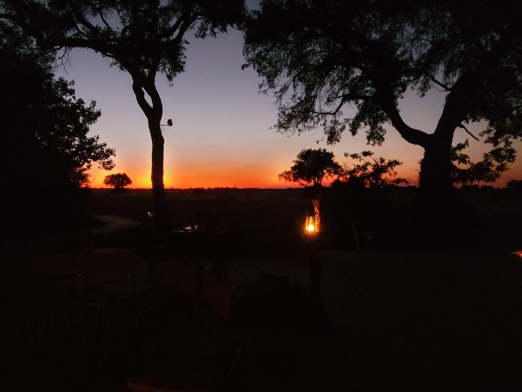 Botswana safari: orange sunset from camp deck with lantern
